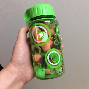 Dry sensory jar full of pompoms, googly eyes, and glitter